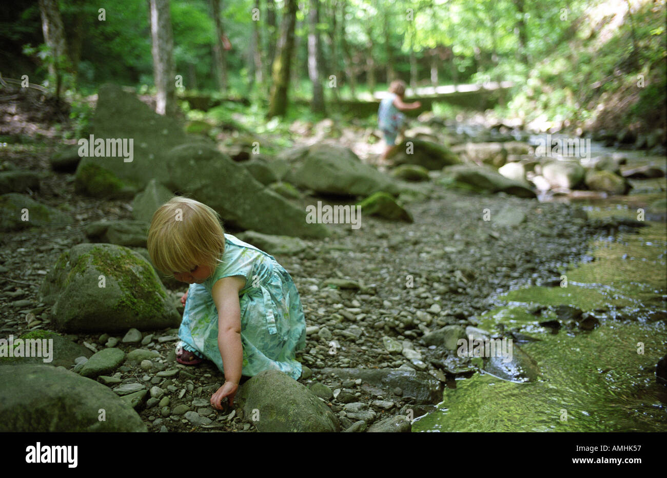 two girls in blue dresses play in dappled woodland by a stream Stock Photo