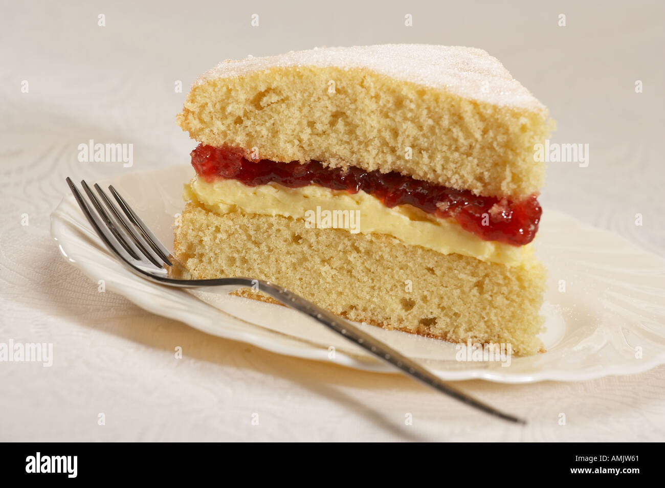 SLICE OF CREAM AND JAM SPONGE CAKE WITH FORK ON WHITE PLATE Stock Photo