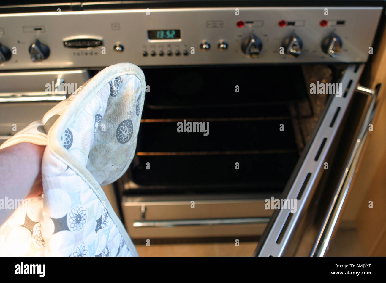 a man with oven gloves on pulling out cooked food from an oven Stock