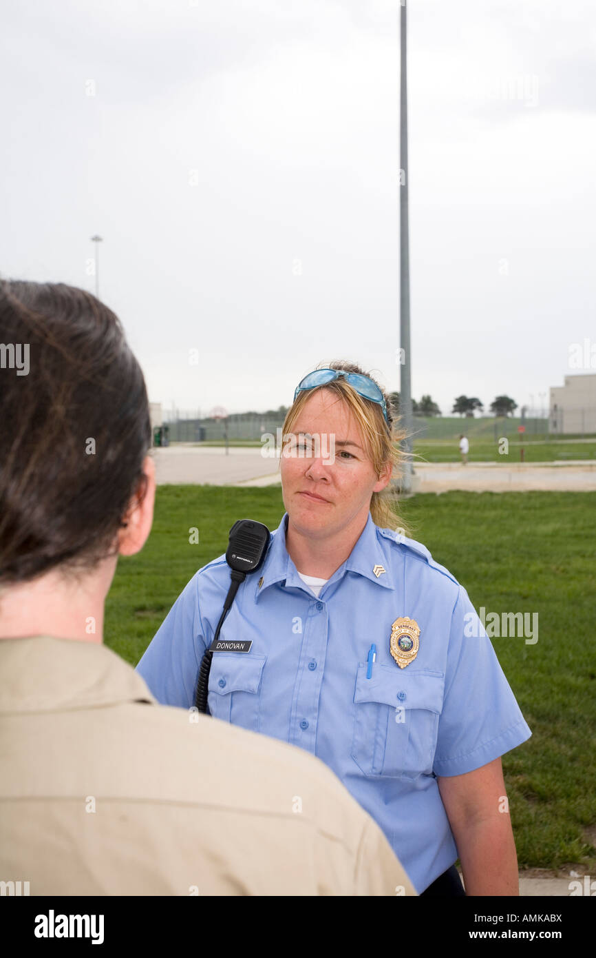 Female Correctional Officer talking to male inmate in the yard of maximum security prison. Stock Photo