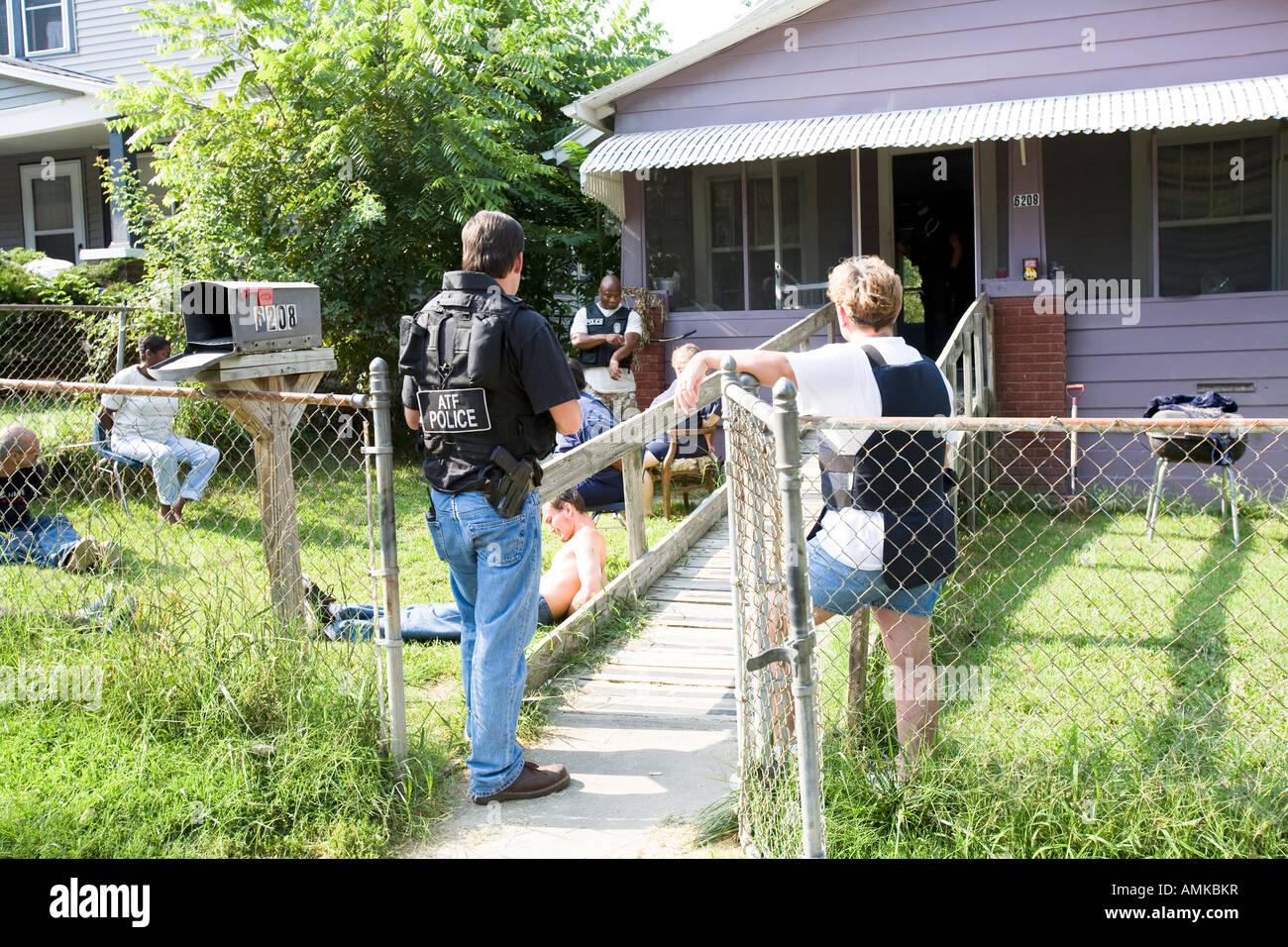 ATF agent and female police officer keeps watch over handcuffed female, narcotics raid. Kansas City, Missouri. Stock Photo