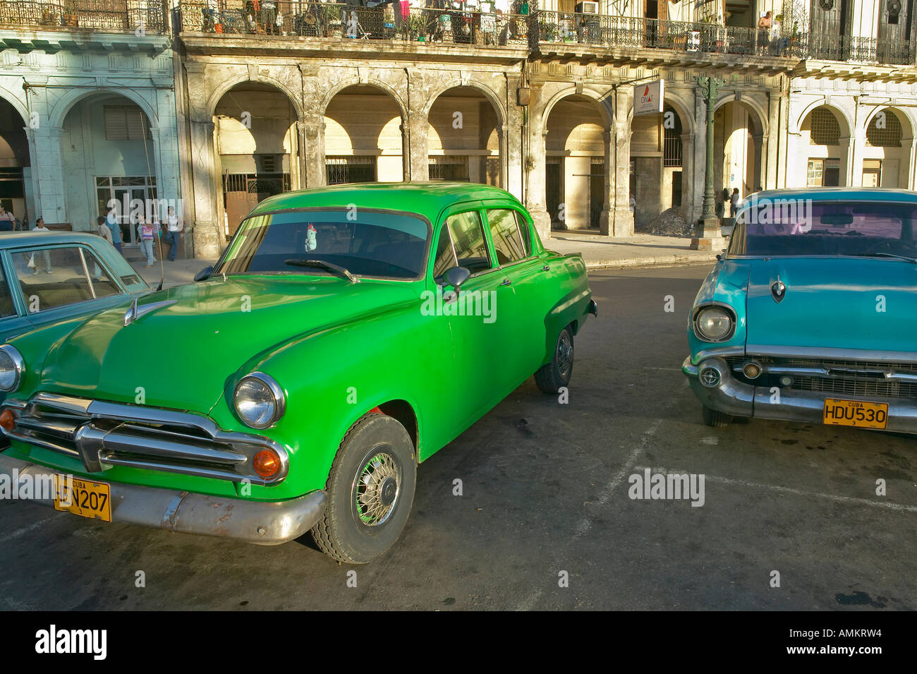 Old green and turquoise American cars are parked in front of old buildings in Old Havana Cuba Stock Photo
