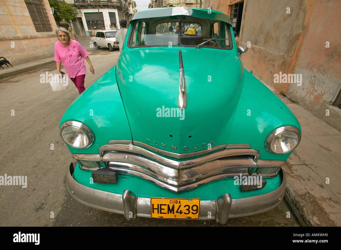 A woman walking in front of turquoise old Dodge parked in front of old buildings in Havana Cuba Stock Photo