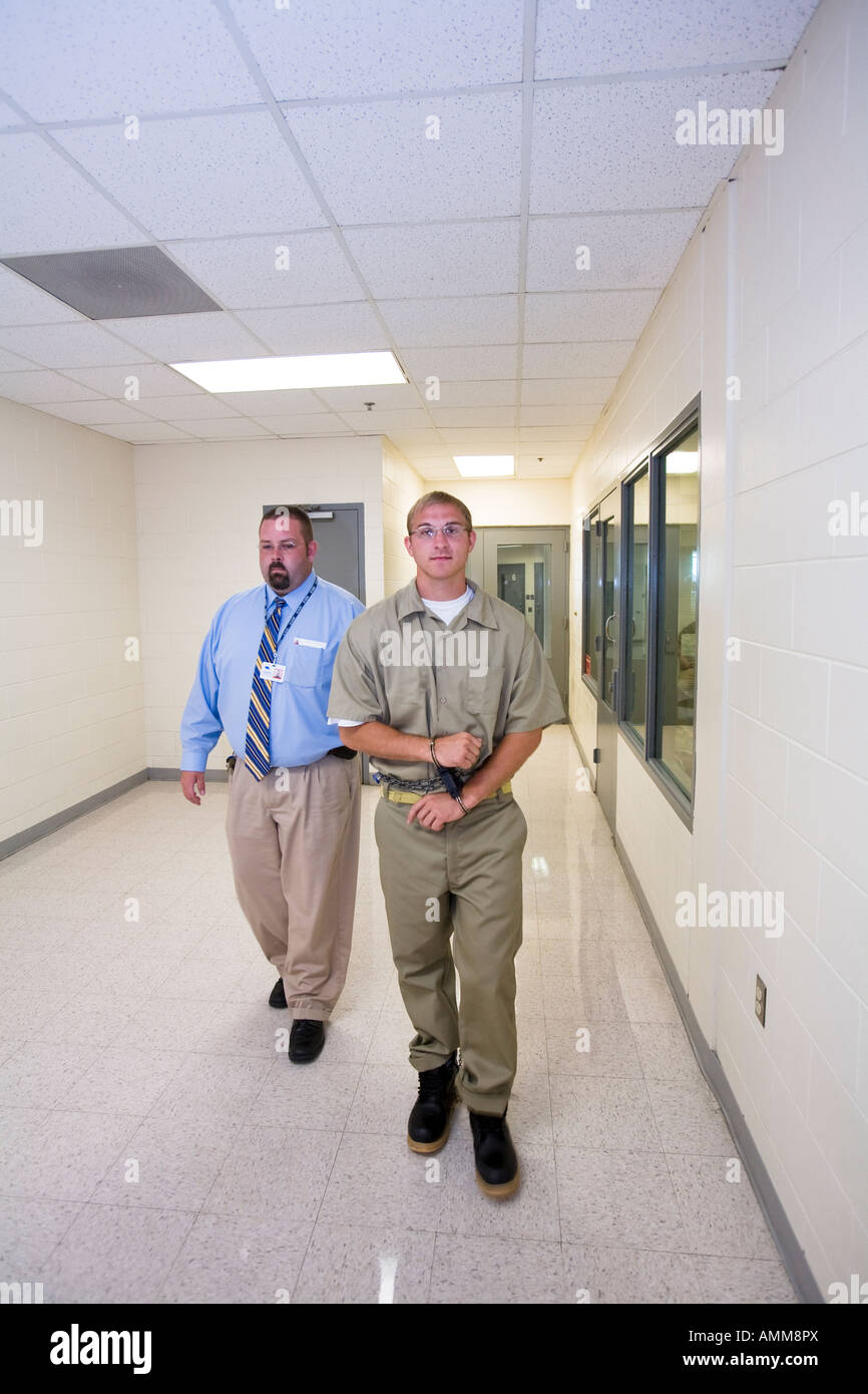 Inmate in full restraints being escorted by transport staff. Stock Photo