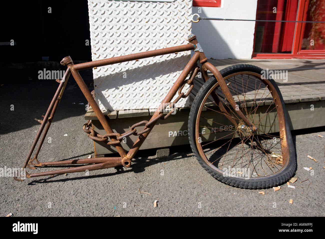 rusty-bicycle-frame-with-one-wheel-locked-to-wall-brittany-france-AMMFPJ.jpg