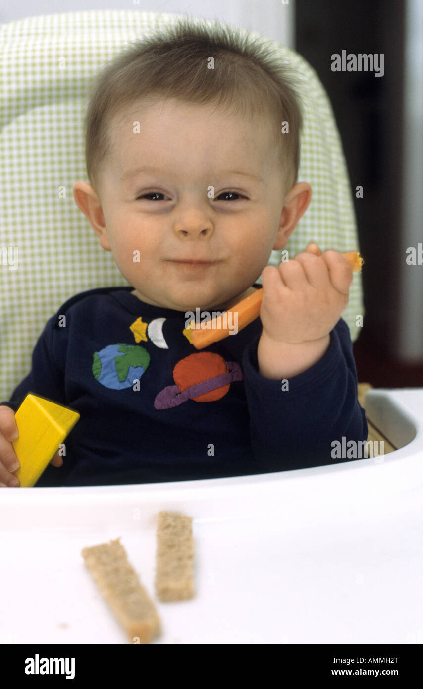 seven month old baby boy sitting in a high chair eating finger food