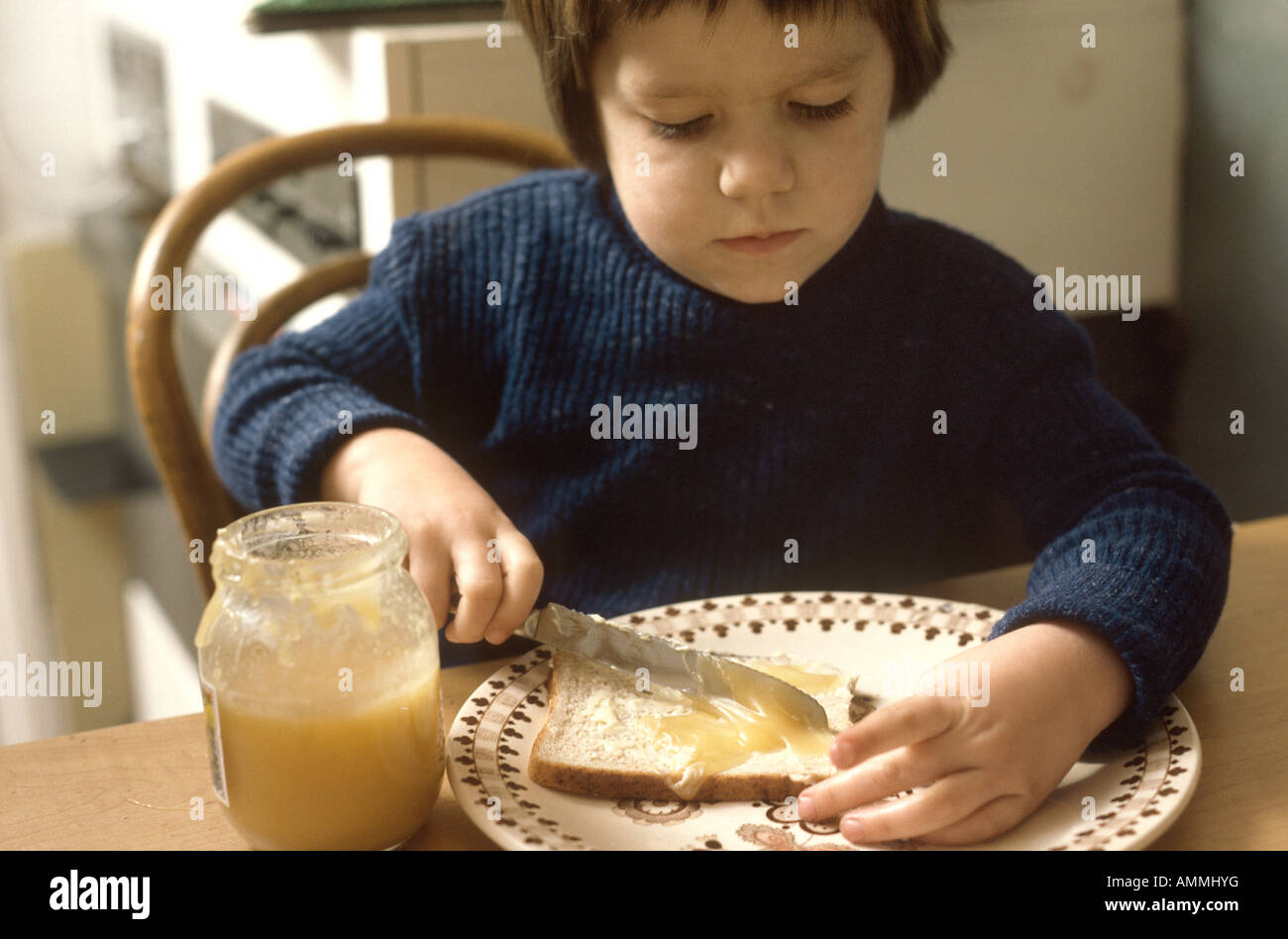 Four year old girl adding honey to her bread using a butter knife Stock