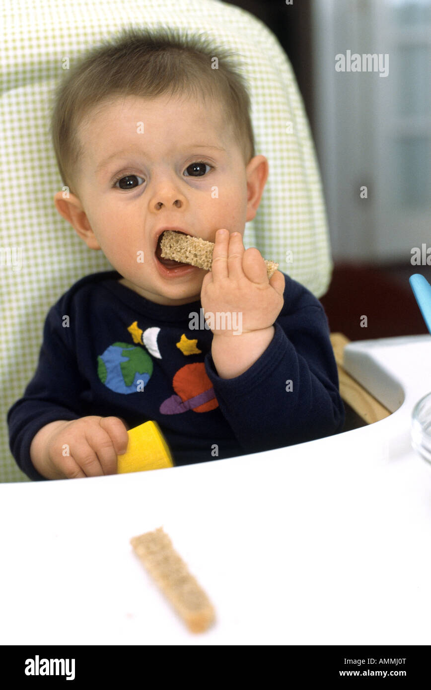 seven month old baby boy sitting in a high chair eating finger food