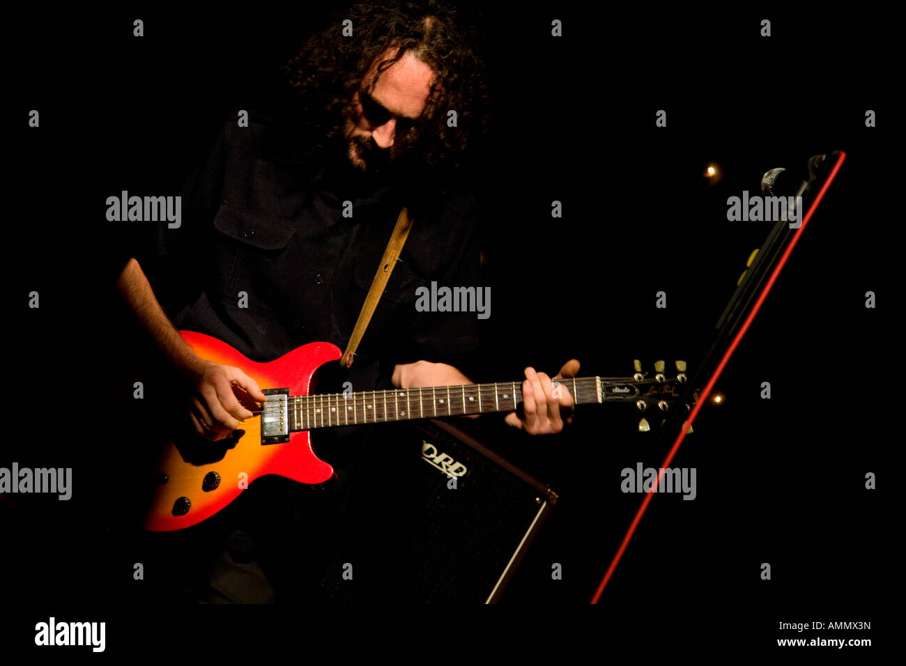 Guitarist playing live at a gig. Band - King Size Slim. Red and yellow guitar shines in the dark. Stock Photo