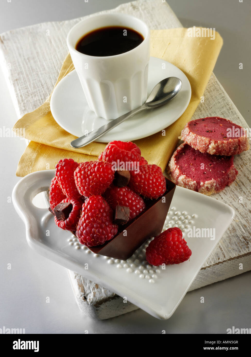 Chocolate cake filled with chocolate topped with fresh raspberries in a cafe setting with coffee Stock Photo