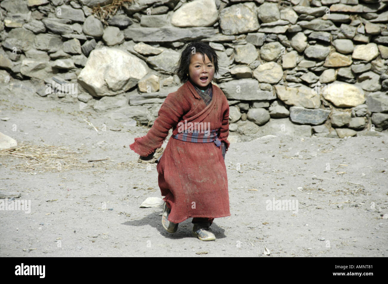Girl dressed in a simple red coat runs along a wall Phu Nar Phu Annapurna Region Nepal Stock Photo