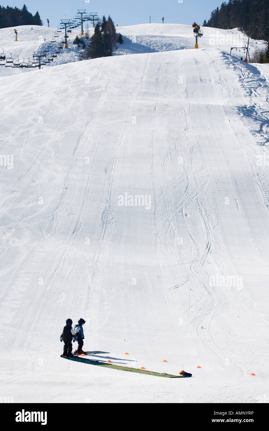 two small children on a learning to ski at the bottom of a long piste Stock Photo