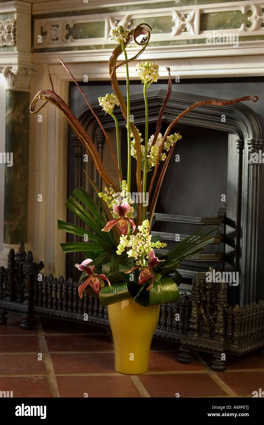 Tall display of orchids with other flowers and leaves in front of antique cast iron Georgian fieplace Stock Photo