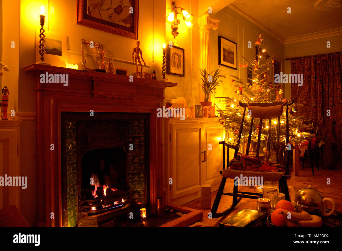 A rocking chair by an open fire with Christmas tree and candles Stock Photo