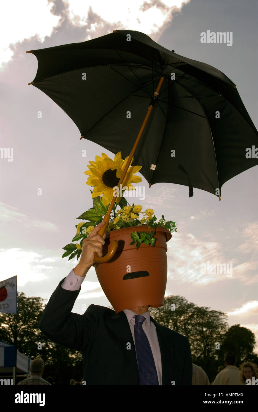 Man with flower pot on head holding umbrella at Hampton Court Show. Stock Photo