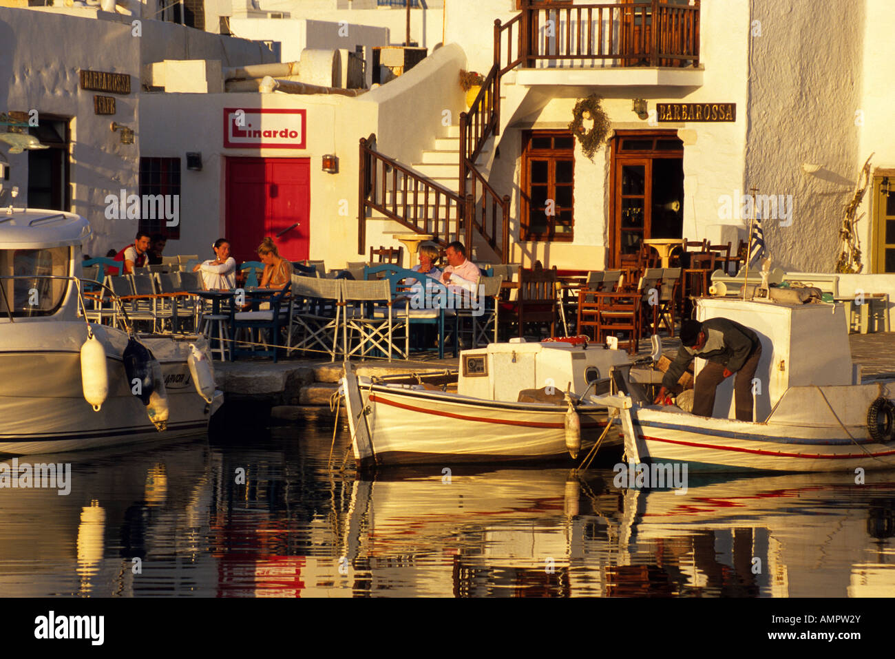 Fishing boats docked next to tavernas on the inner harbor of the Greek Isles town of Naoussa Stock Photo