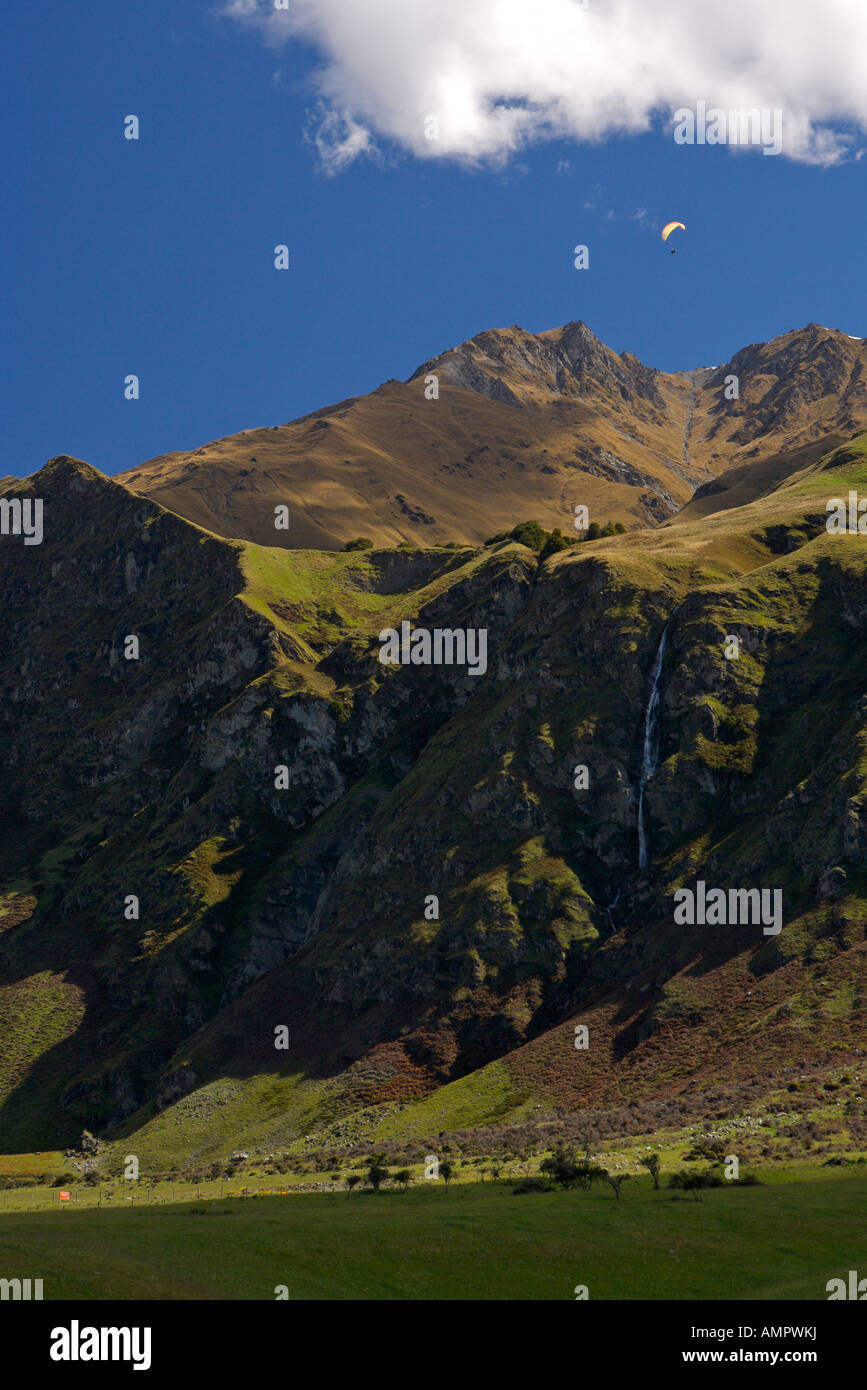 Paraglider near a waterfall on Treble Cone, Harris Mountains, Central Otago, South Island, New Zealand. Stock Photo