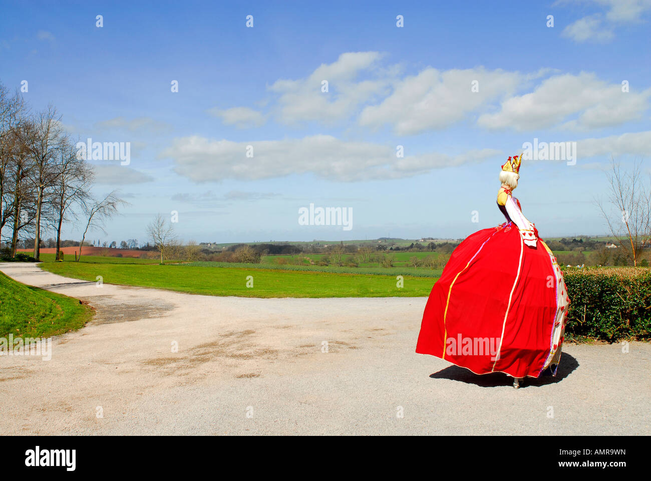 Woman dressed as queen in red dress and wearing crown walking on stilts