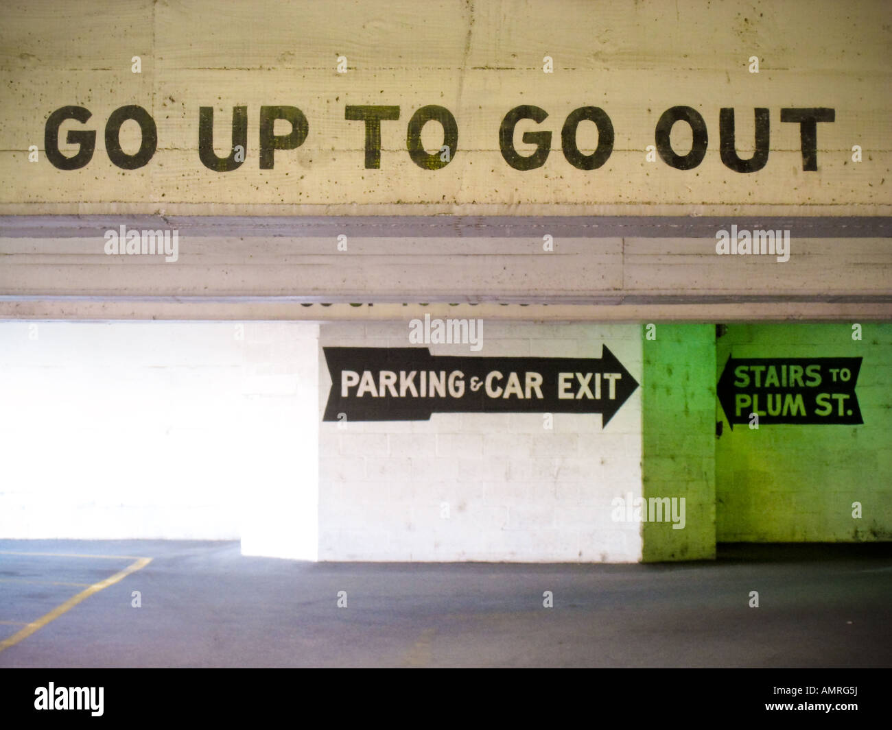 Go up to go Out - painted in black with a stencil on the cement header of a parking garage. A large arrow guides to the exit. Stock Photo