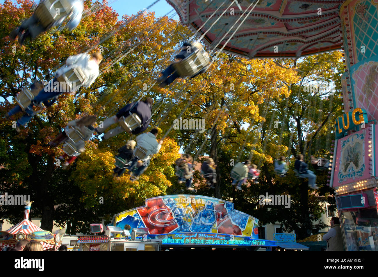 Blurred motion rapid people riding the chairoplane in front of autumn leaved trees parish fair Auer Dult Mariahilfplatz Au Stock Photo