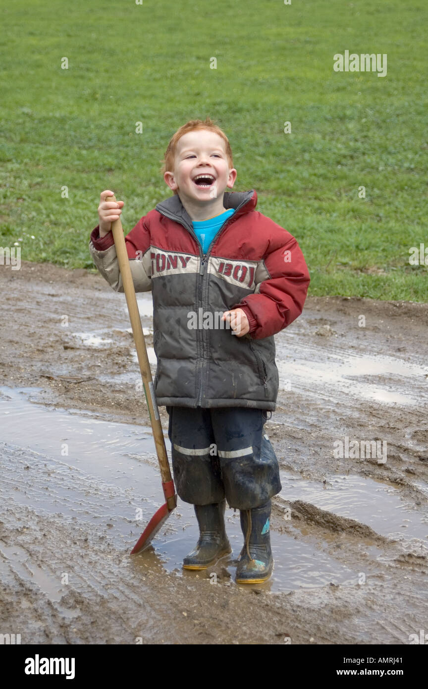 MR Junge spielt an einem Regentag mit einer Schaufel im Matsch MR boy plays and has fun on a rainy day with a spade in the mud Stock Photo