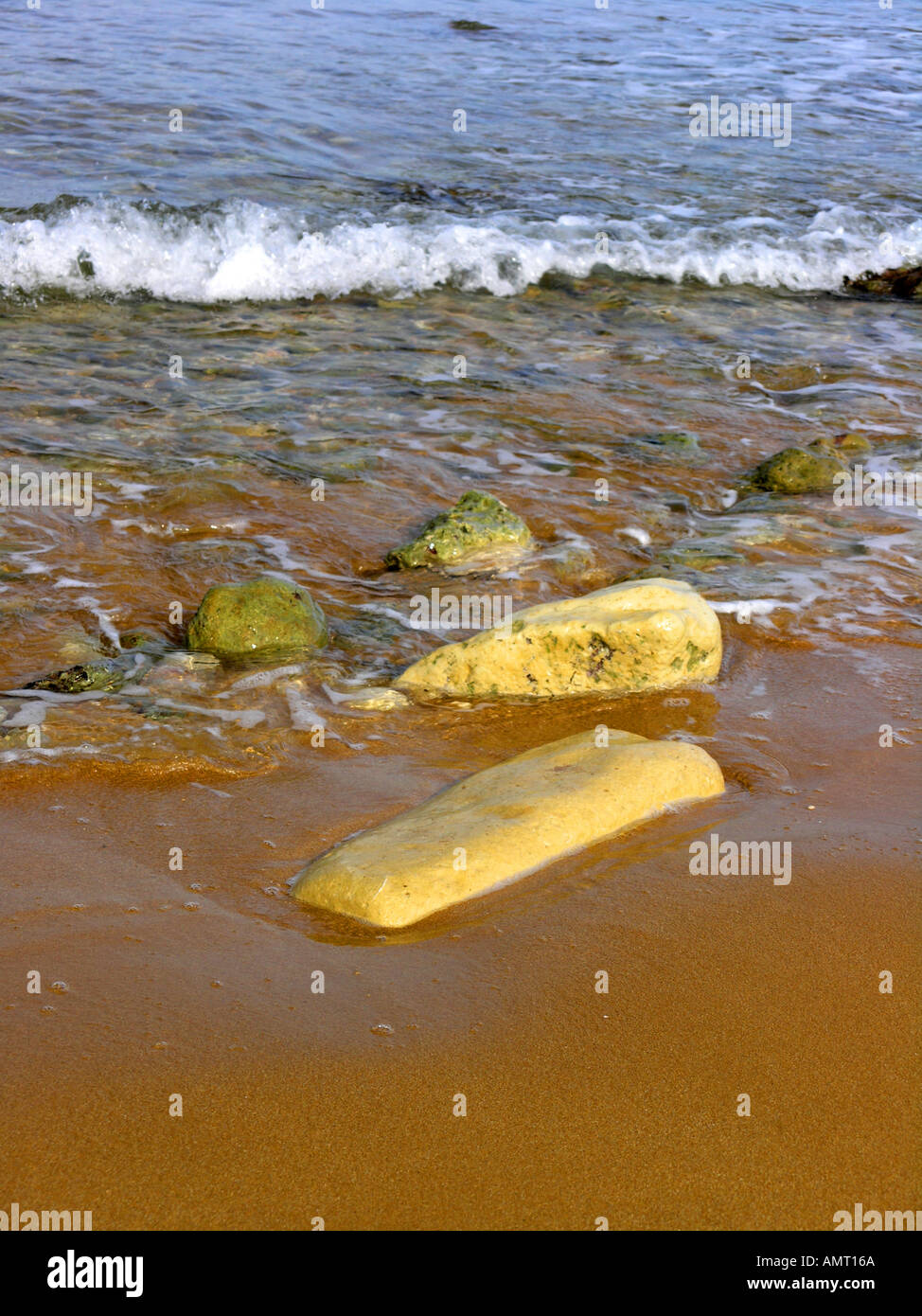 Wave and rocks on a sandy beach Stock Photo - Alamy