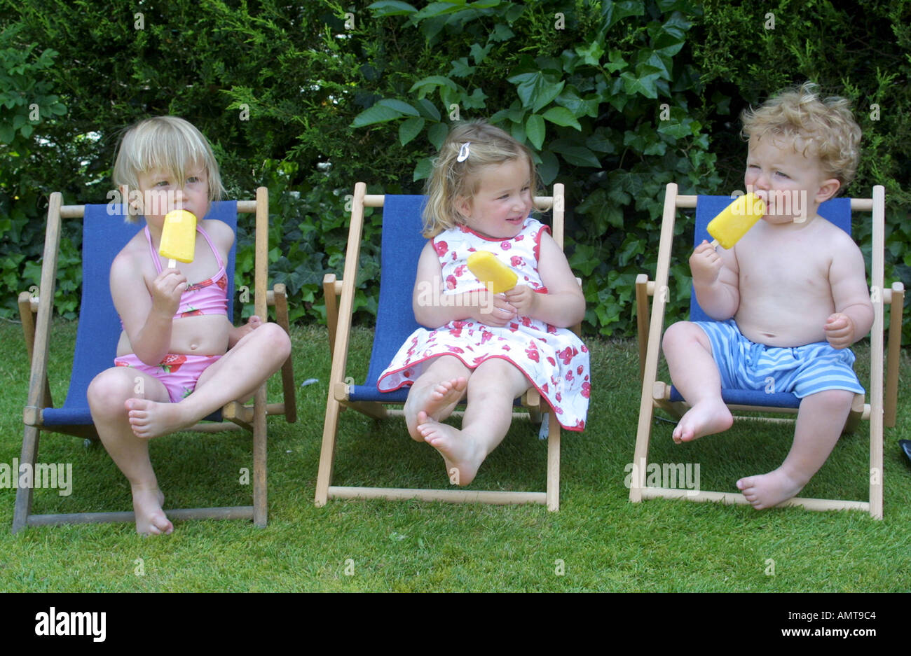 Two young girls and a boy eating lollies while sitting outside on  deckchairs Stock Photo - Alamy
