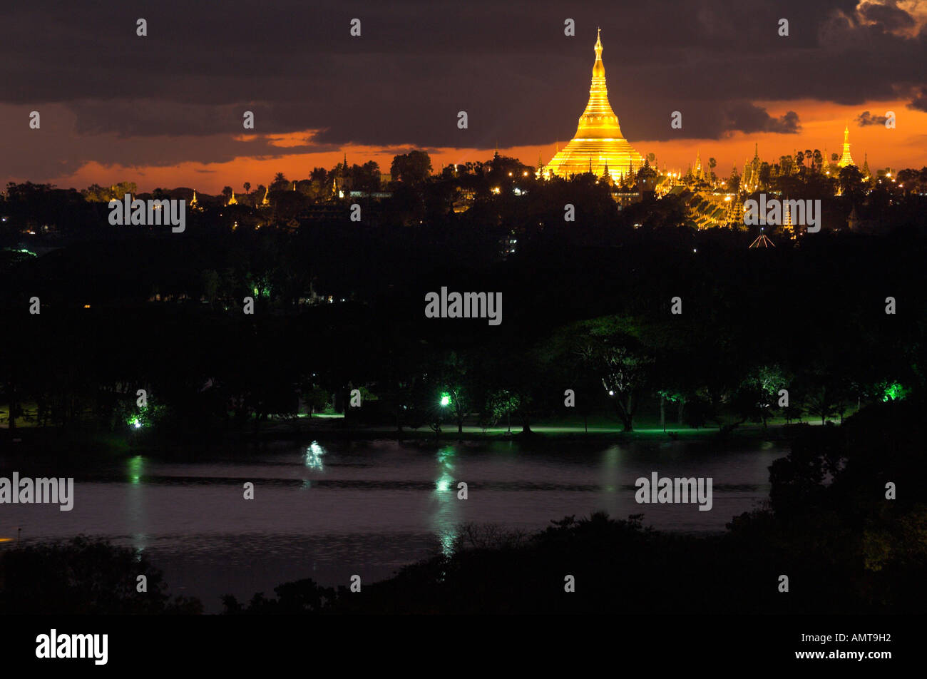 Myanmar Burma Yangon Shwedagon Paya at dusk with Kandawgyi lake in frgd view from afar with lit up pagoda and dramatic sky Stock Photo