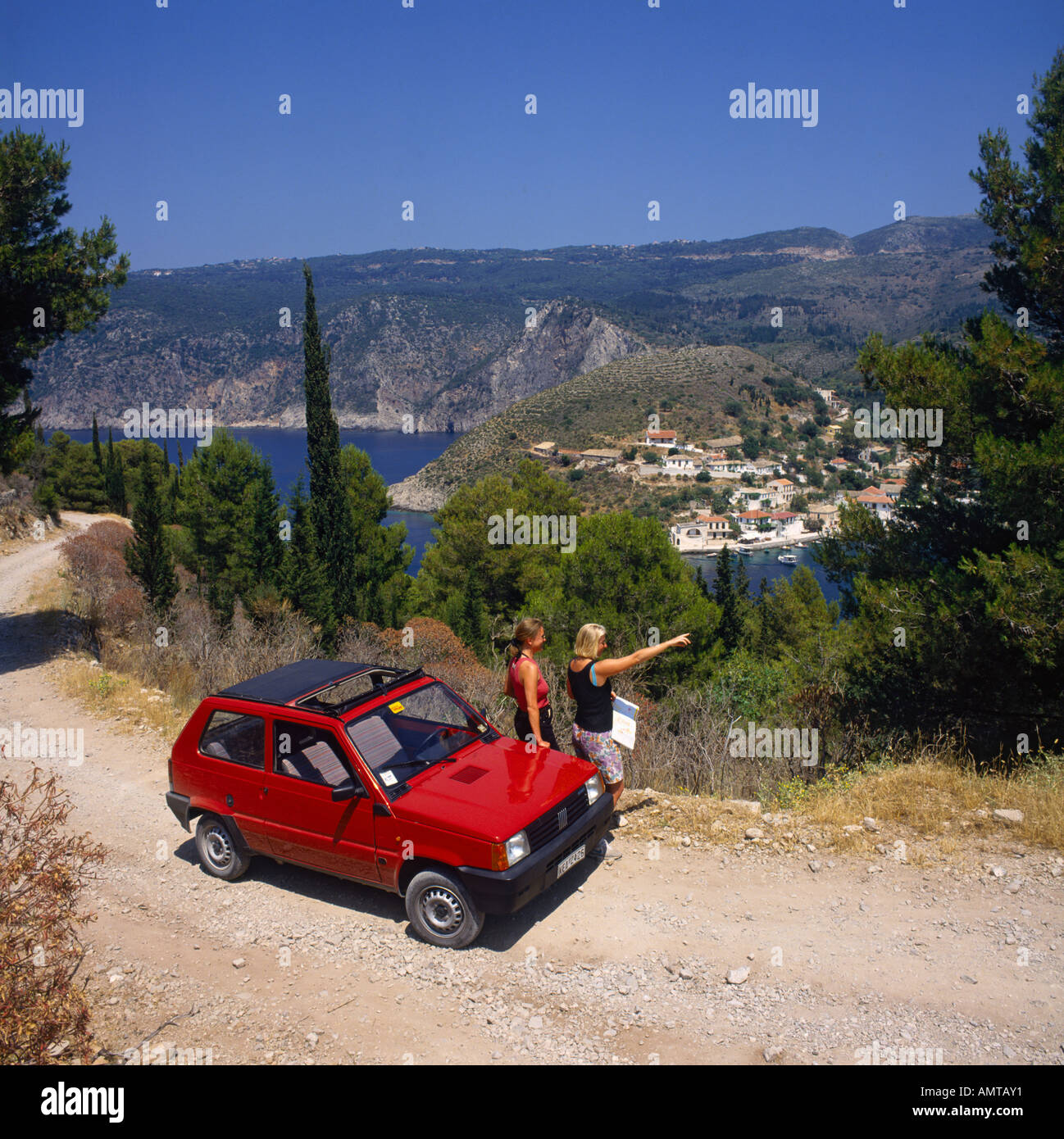 Two girls standing by red hire car reading a map and overlooking sea at