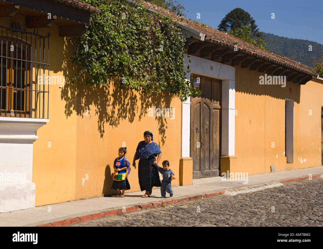 Local woman with two children walking down sunlit cobbled street in Antigua city in the Republic of Guatemala Central America Stock Photo