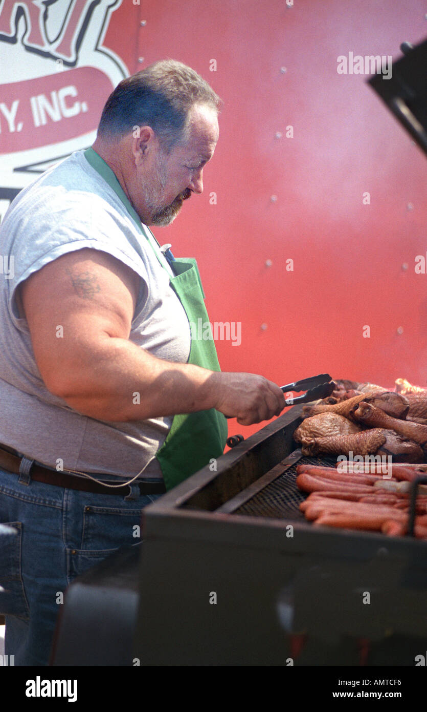 Overweight adult male cooks on a barbeque for a large group of people Stock Photo