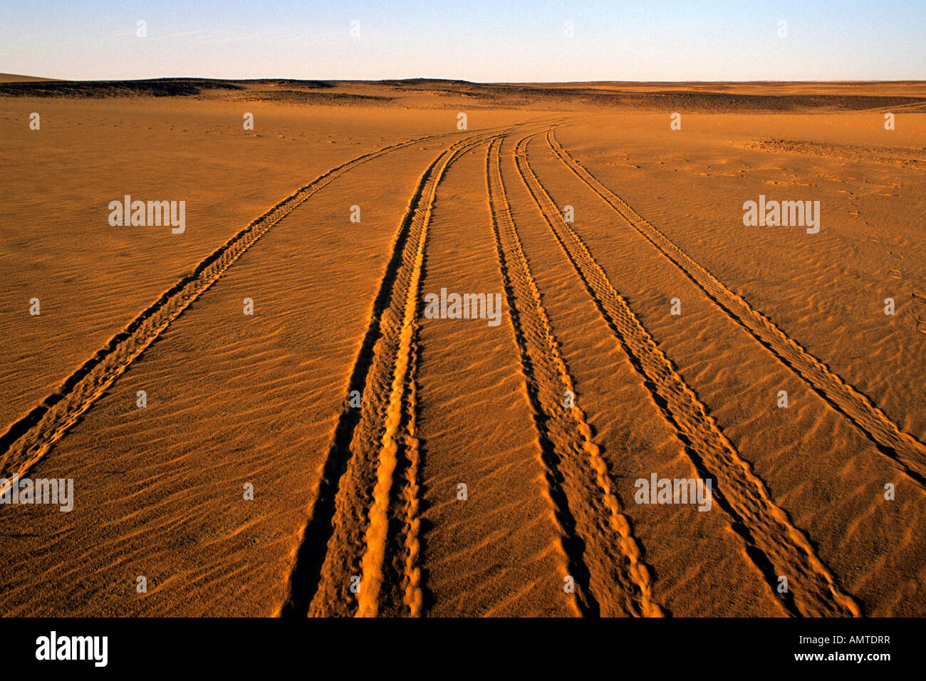 The rippled sands of a flat stretch of the Sahara desert are broken by