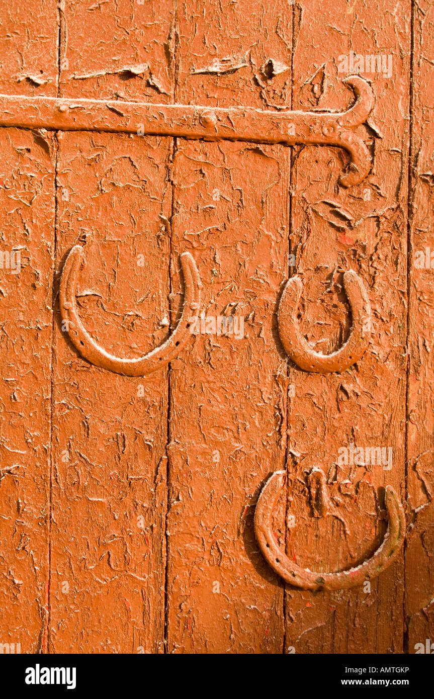 Red painted barn door on farm; three horseshoes nailed on to the door