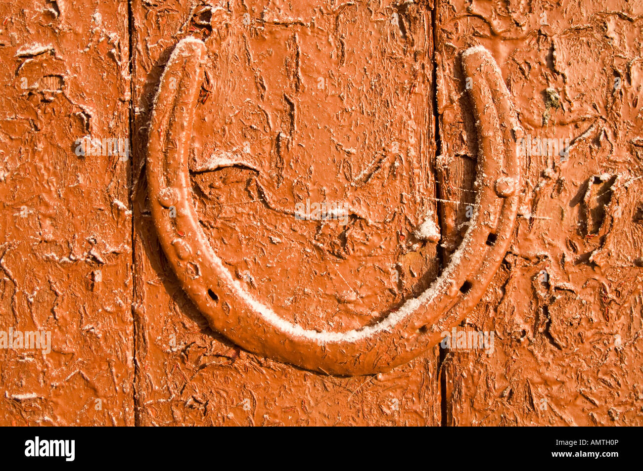 Horseshoe nailed to a barn door and painted red; flakes of snow on it. Stock Photo