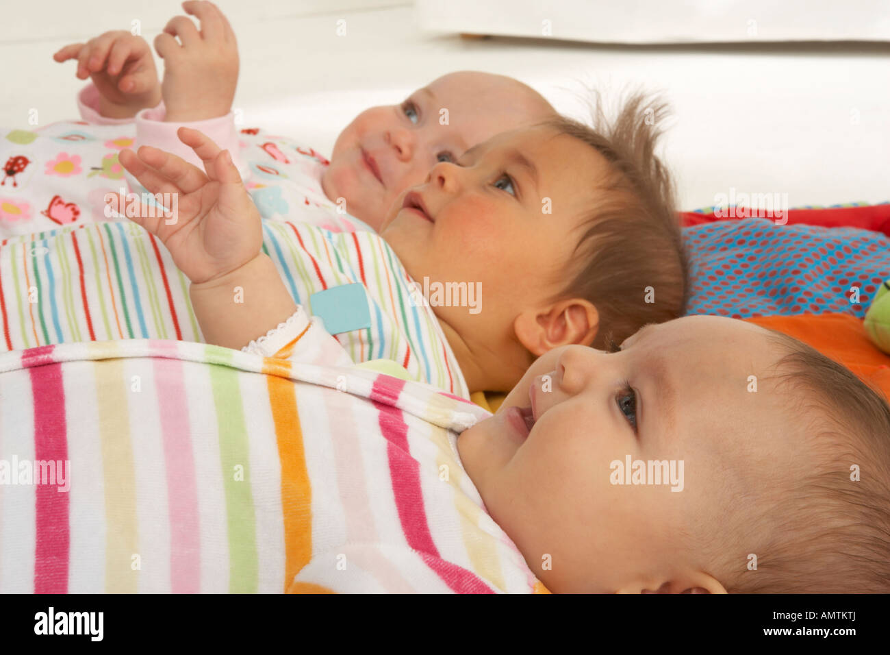 Three babies lay side by side on their backs in profile and smile as