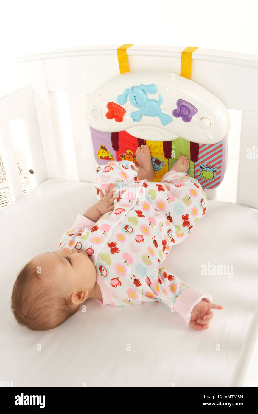 A baby lays on its back in a cot and uses its feet to play with a toy