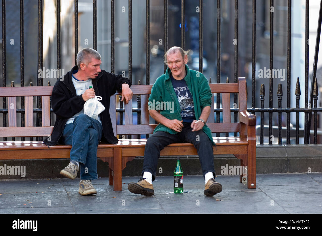 Two adult men sitting on a bench talking and drinking Stock Photo - Alamy