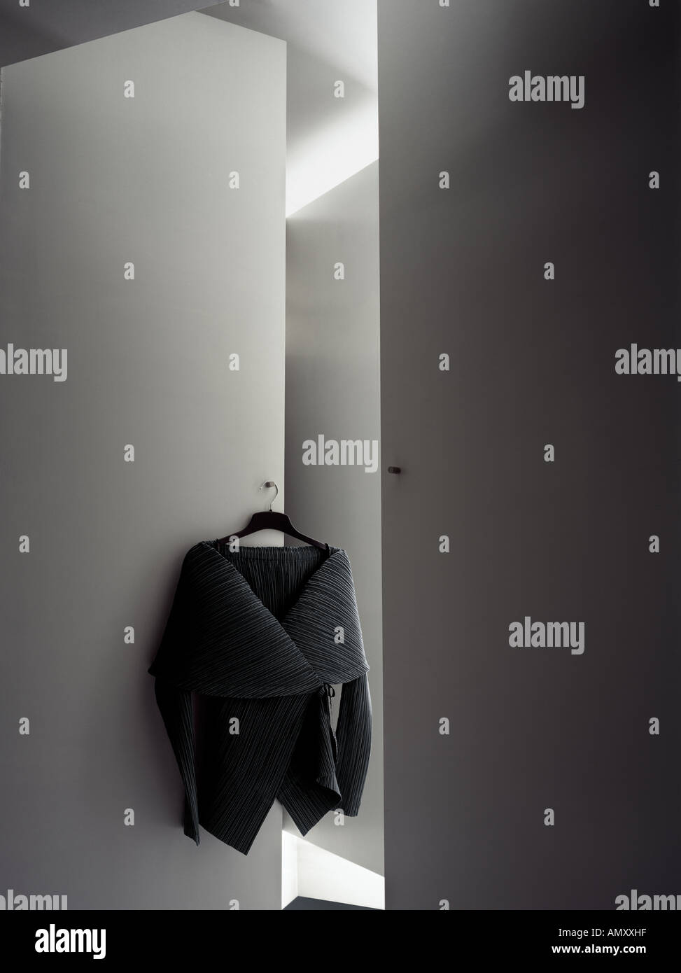 Black Issey Miyake jacket hanging on a door of wardrobes which form shapes matching cut of the garment Stock Photo