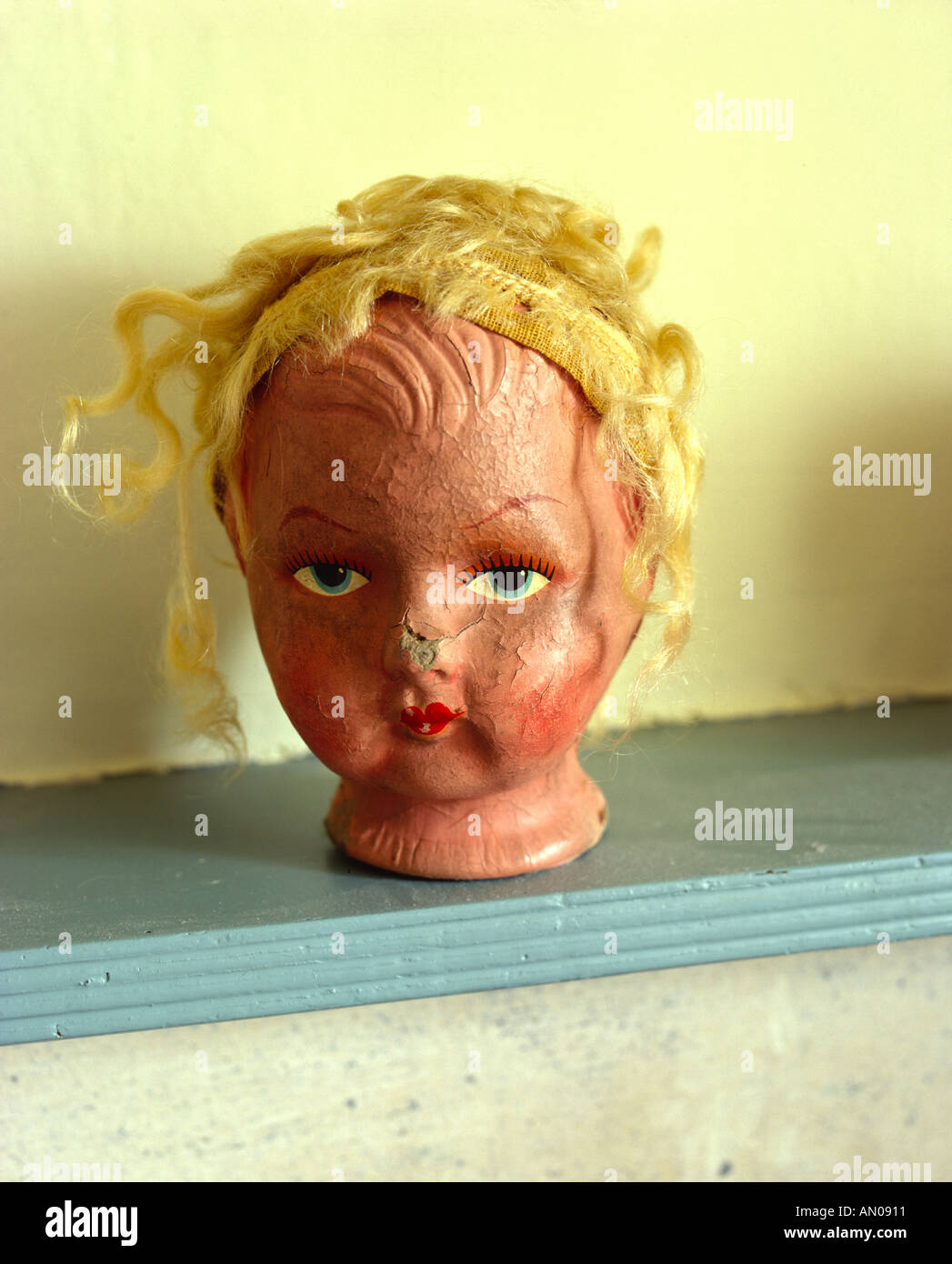 old worn dolls head sitting on shelf with bright fake yellow blonde hair Stock Photo