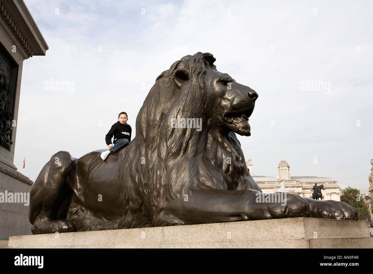 UK London Trafalgar Square young boy sat on Landseers Lion at base of Nelsons Column Stock Photo