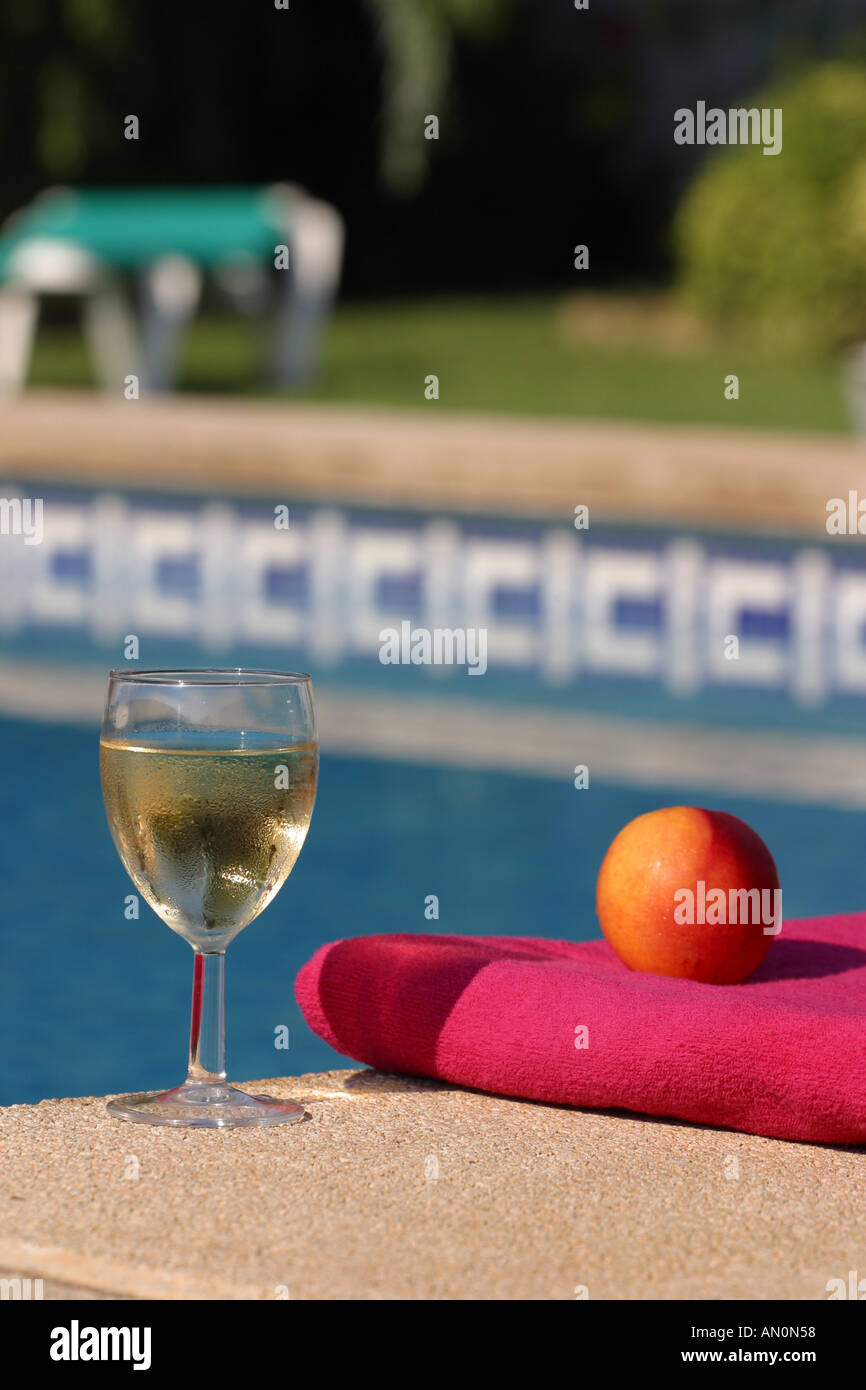Holiday glass of wine fresh fruit and towel next to swimming pool Stock Photo