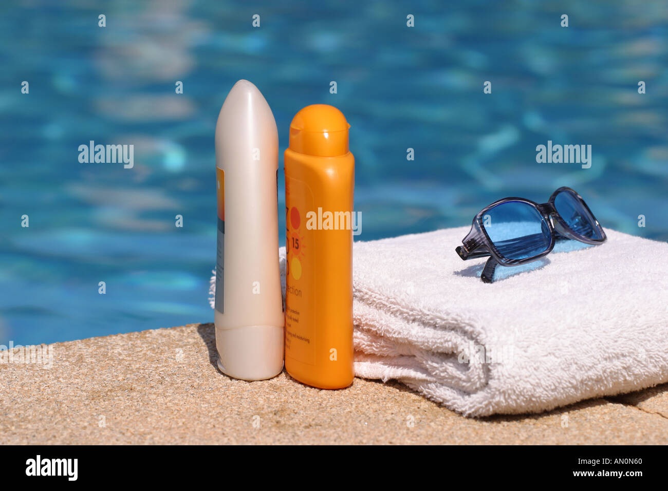 Holiday Sun cream sunglasses and towel next to swimming pool Stock Photo