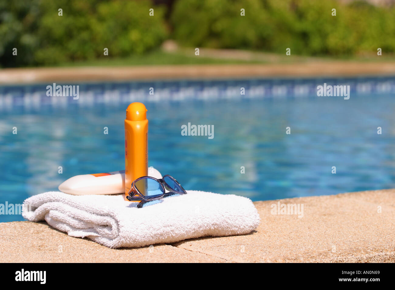 Holiday Sun cream sunglasses and towel next to swimming pool Stock Photo