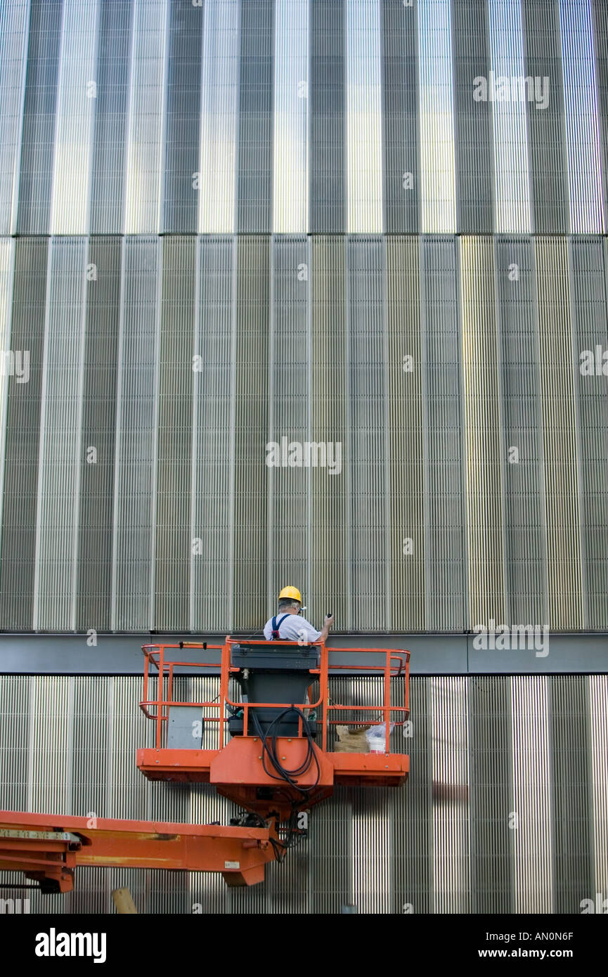 Construction worker wearing yellow hat on orange elevated crane platform in front of metal surface of a skyscraper New York USA Stock Photo