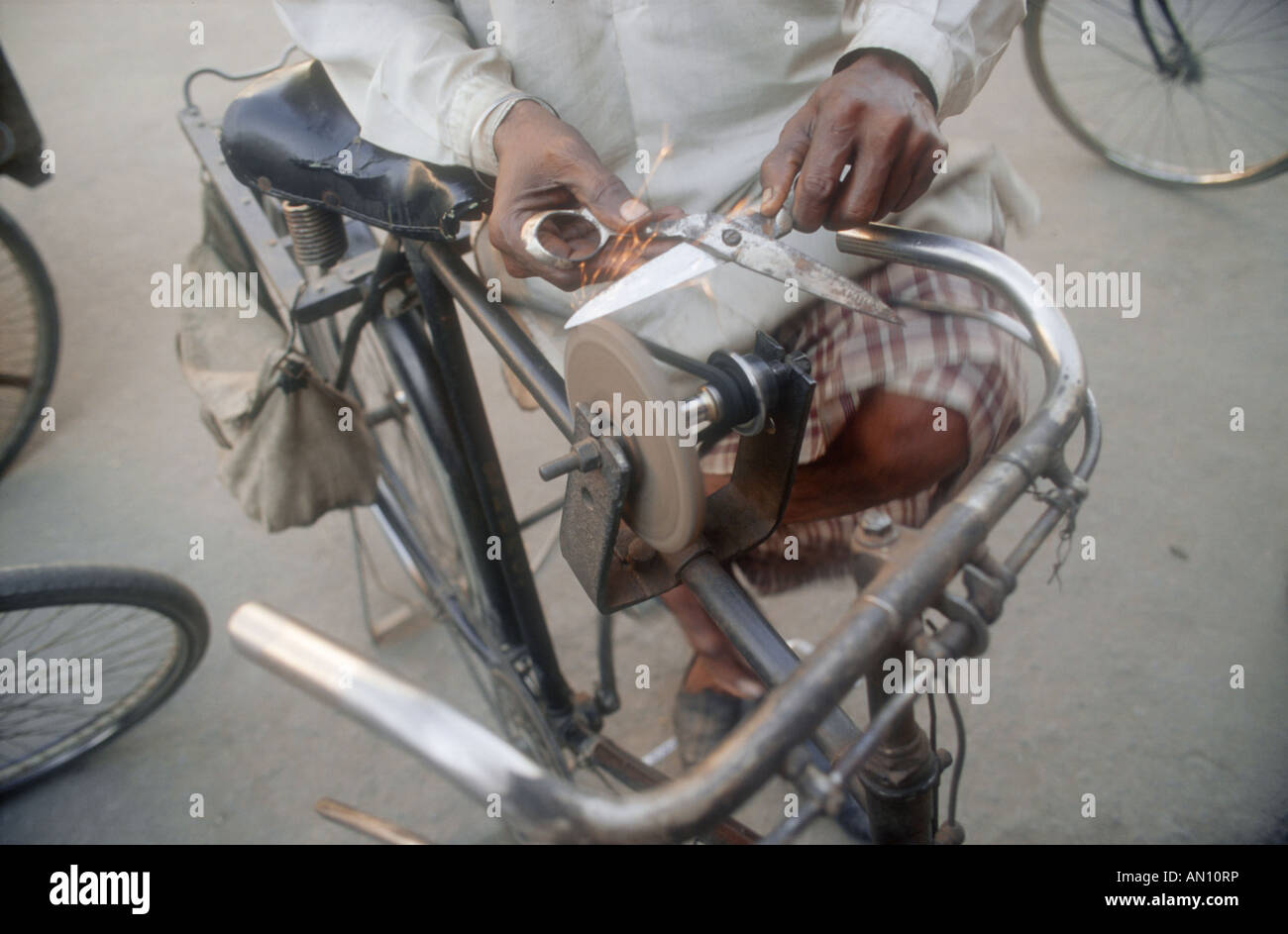 Using a grindstone powered by a bicycle to sharpen a pair of scissors. India Stock Photo