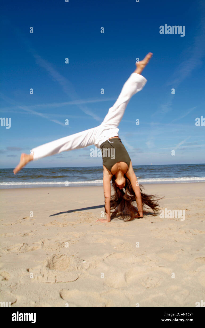 Lifestyle young woman 20+ doing gymnastics and jumping on beach happy