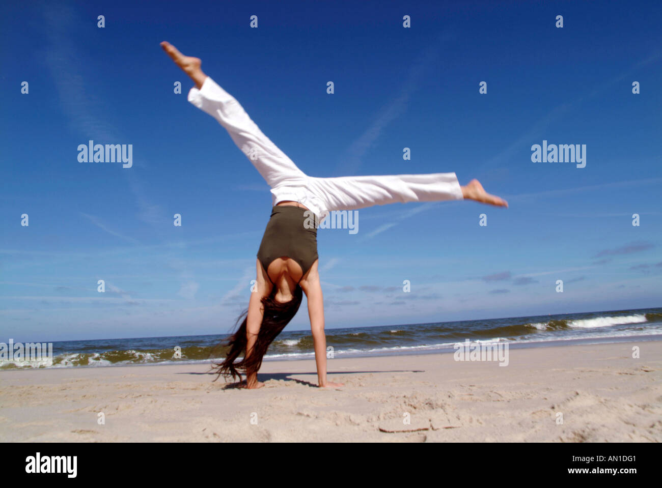 Lifestyle young woman 20+ doing gymnastics and jumping on beach happy