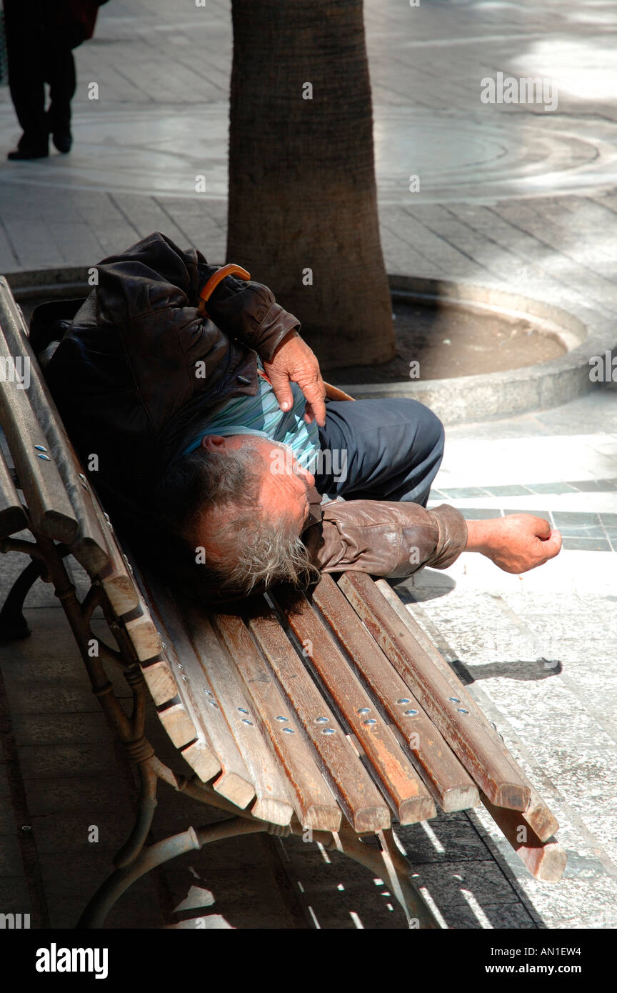 Homeless man sleeping on street bench Stock Photo