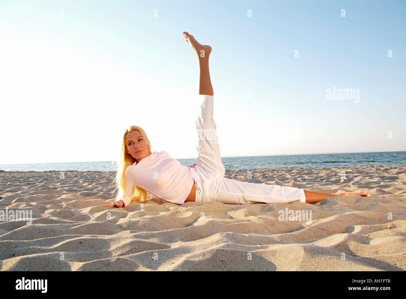 young woman lying at beachfront doing gymnastics in the sand Stock Photo