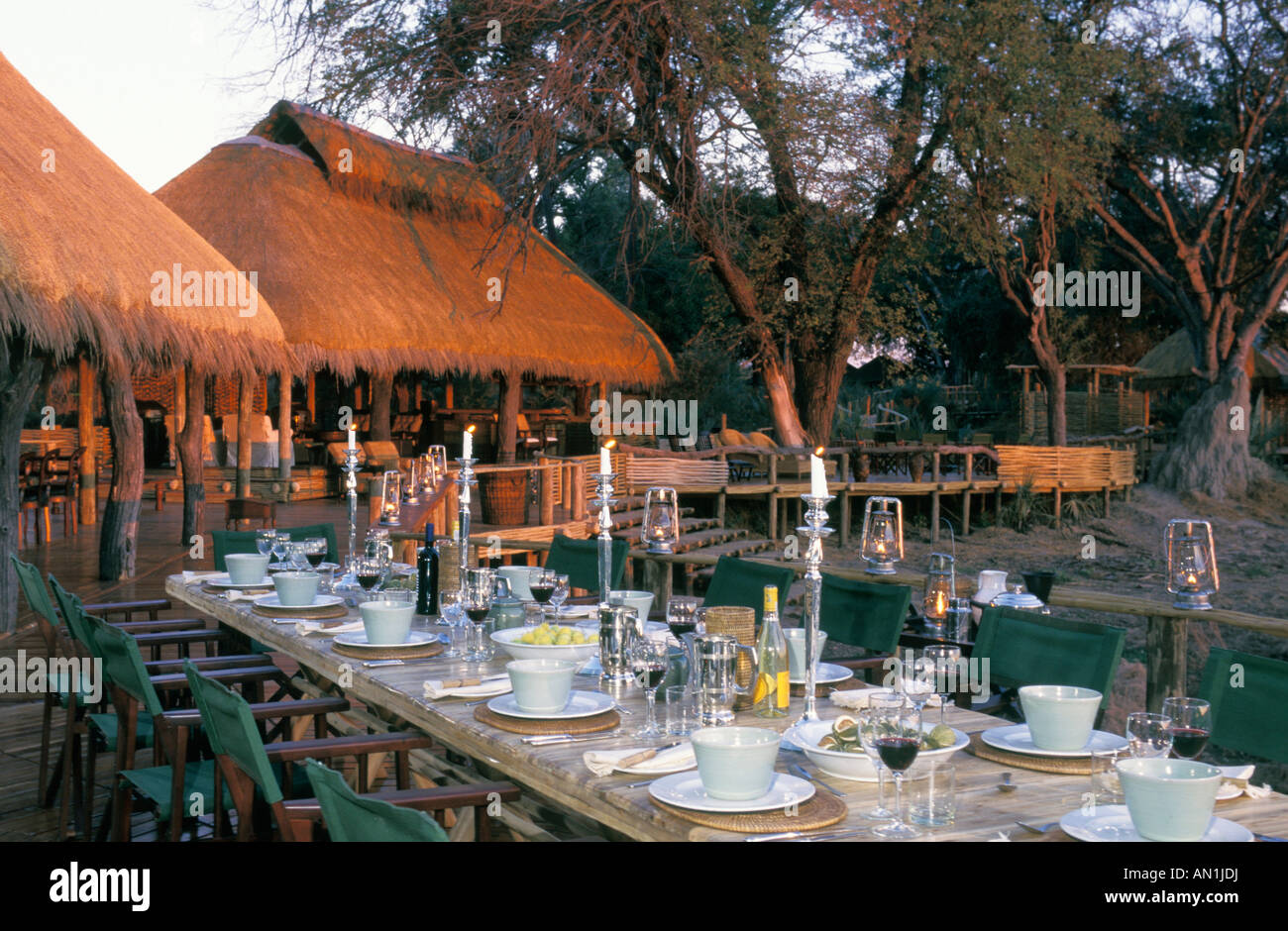 Exterior view of Mombo camp with a long table set outside for dinner replete with candles and wine glasses Stock Photo